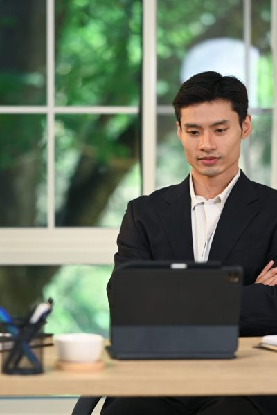 Concentrated businessman sitting at desk with arms crossed, reviews or contemplates his work.